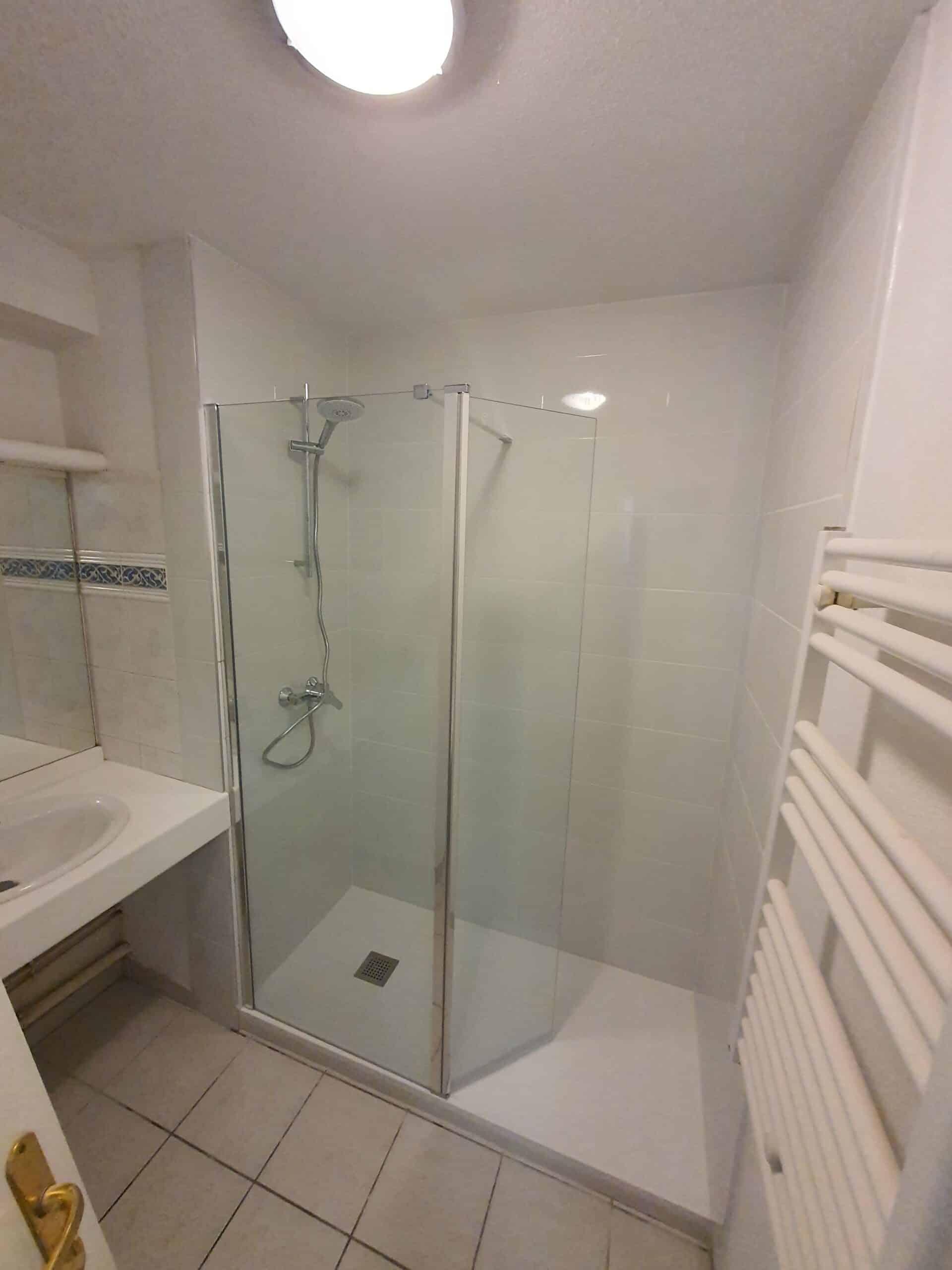 Salle de bain moderne avec douche à l'italienne, cabine vitrée, lavabo intégré et sèche-serviettes blanc.