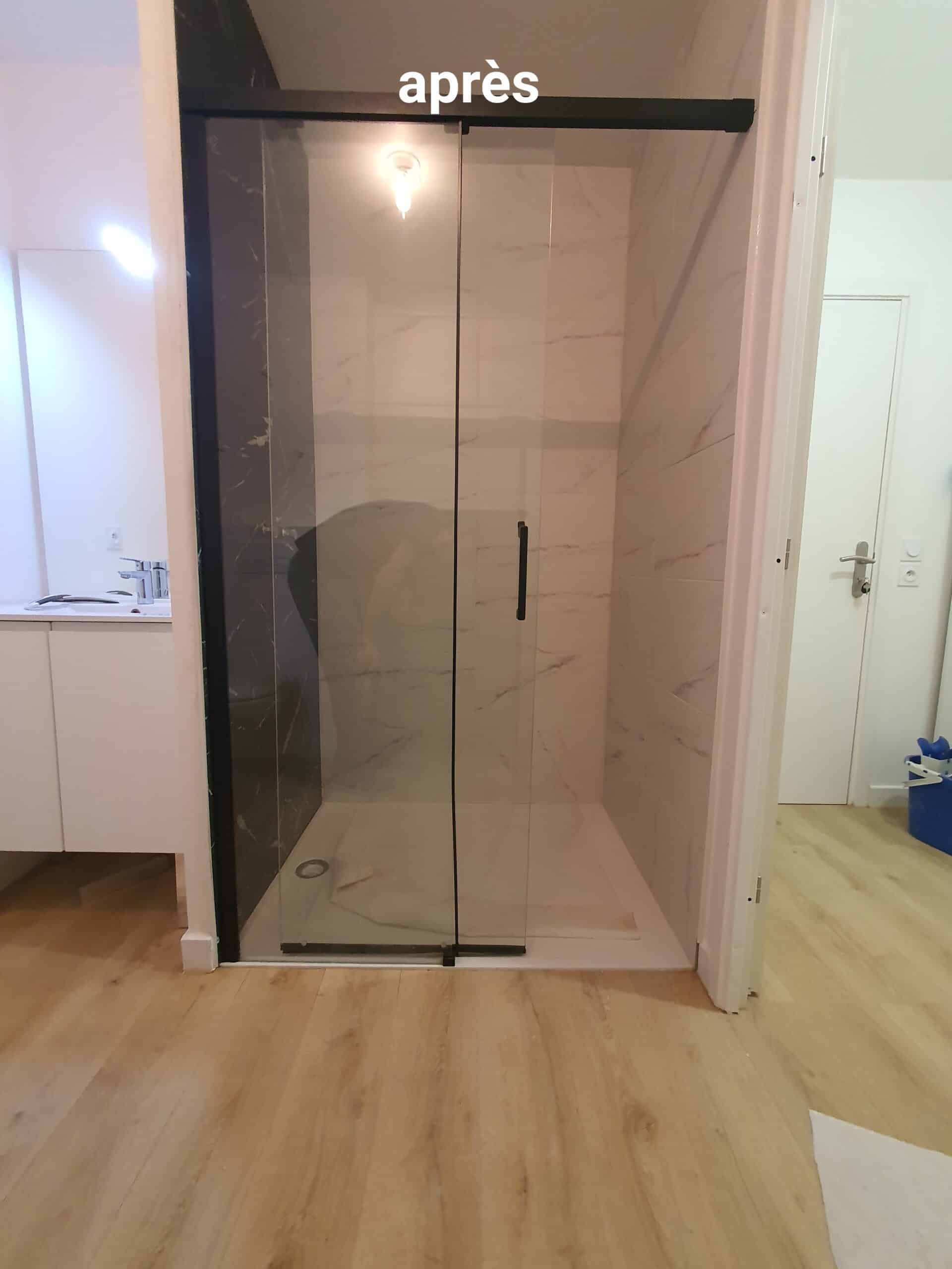 Douche moderne après rénovation avec porte coulissante en verre, parois effet marbre blanc et noir, et sol clair. Texte « après » visible.
