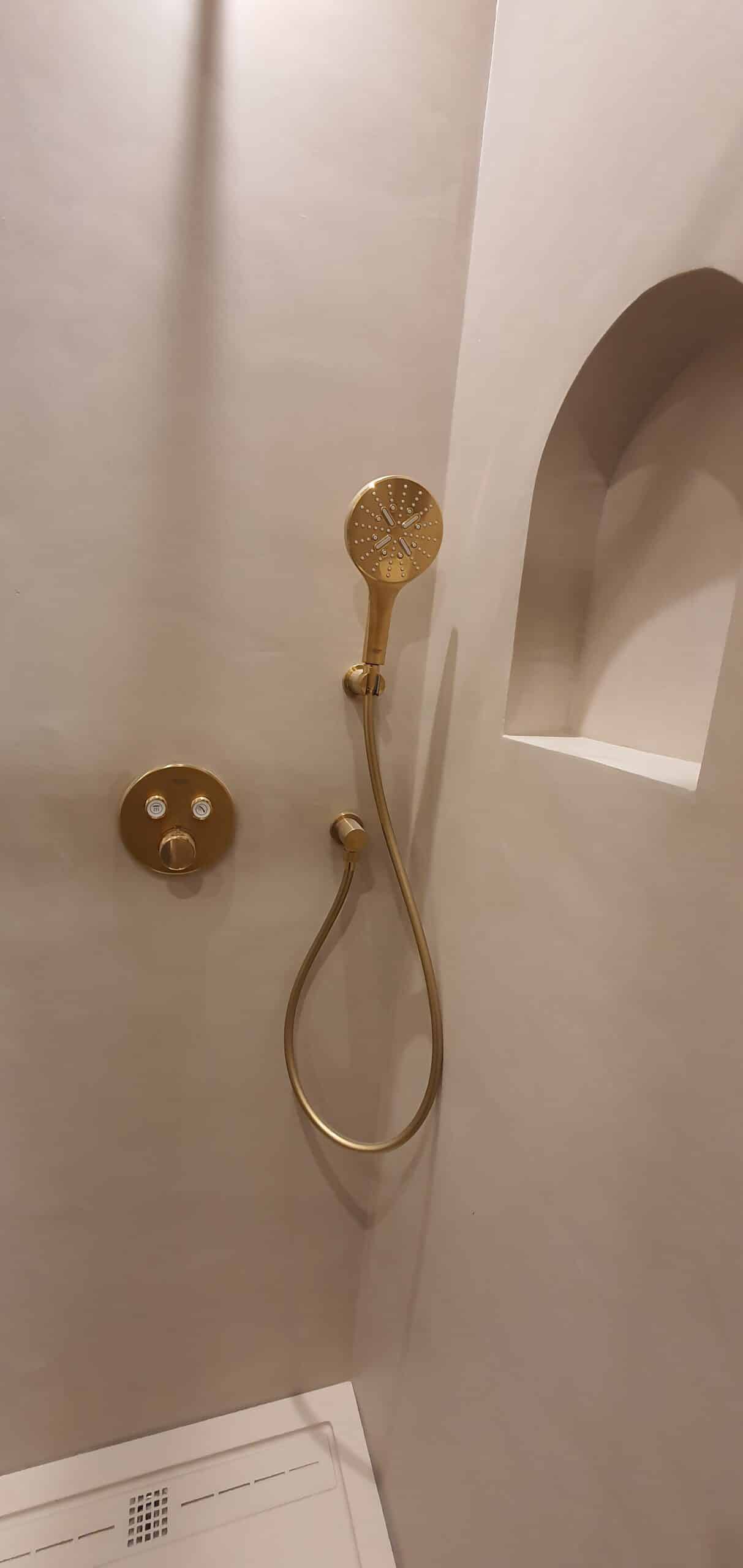 Douche murale moderne finition or brossé avec mitigeur encastré et niche arquée beige.