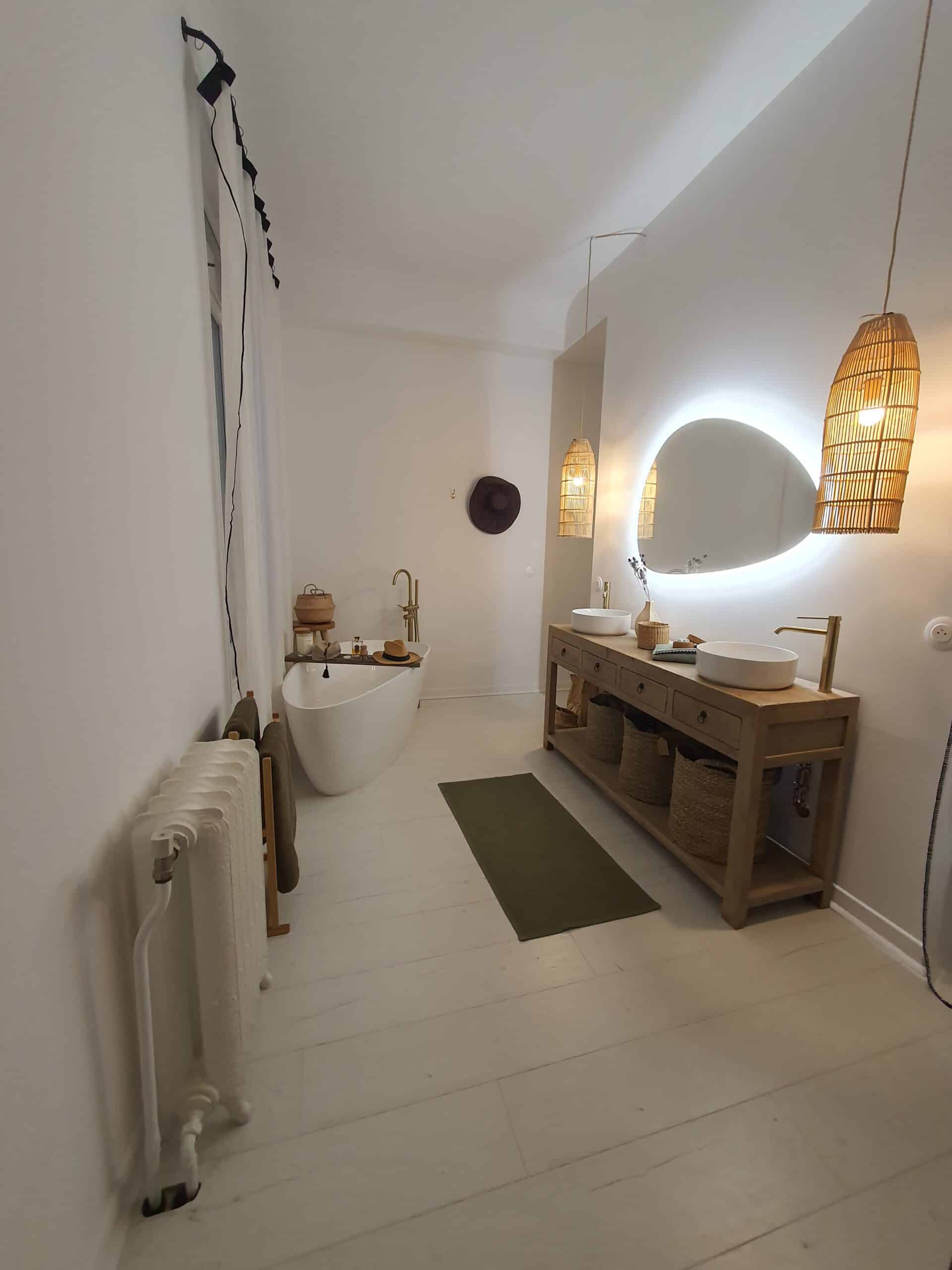 Salle de bain bohème chic avec baignoire sur pied, double vasque en bois, robinetterie or brossé et luminaires en rotin.