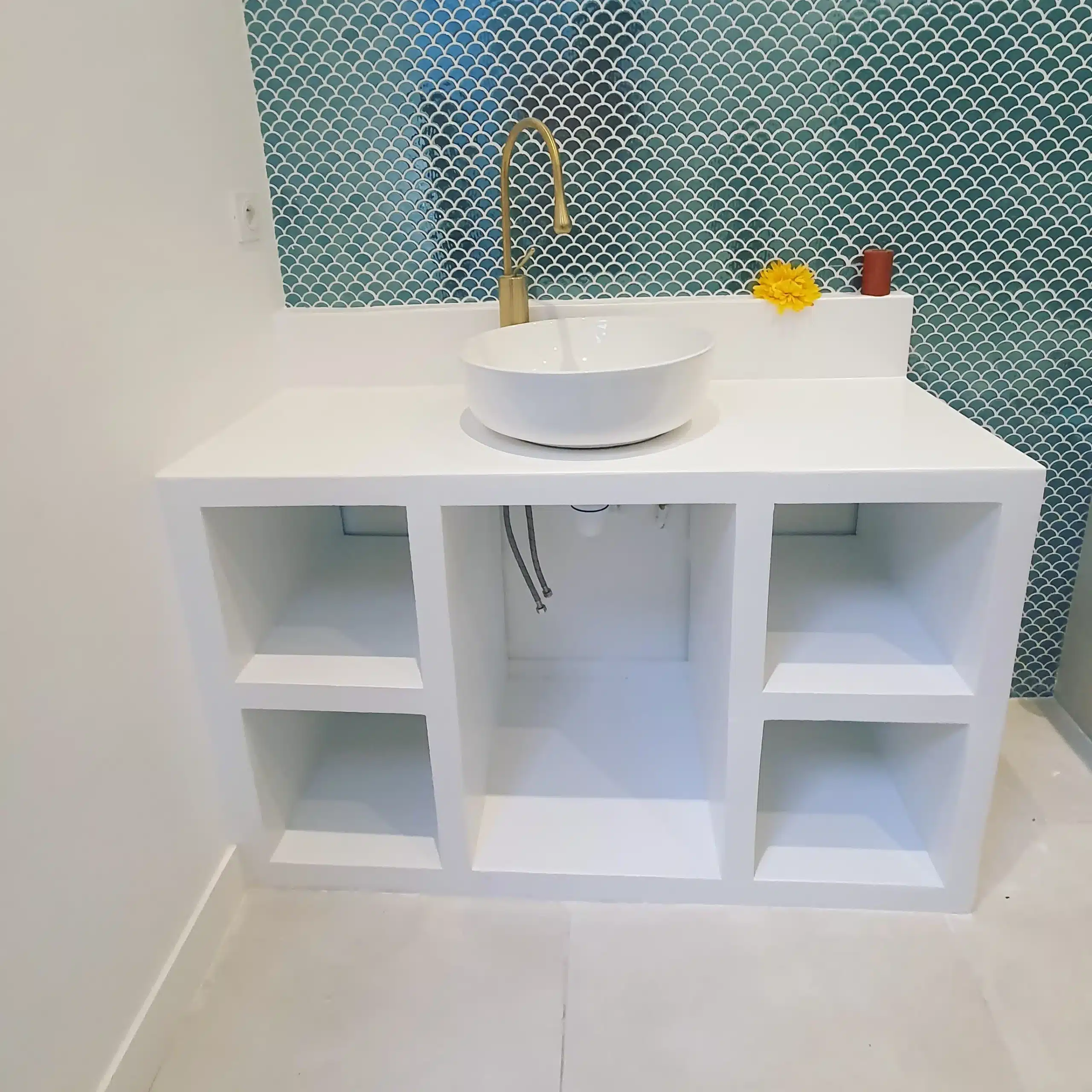 Meuble vasque blanc moderne avec lavabo rond, robinet doré et mur en mosaïque écailles de poisson bleu-vert.